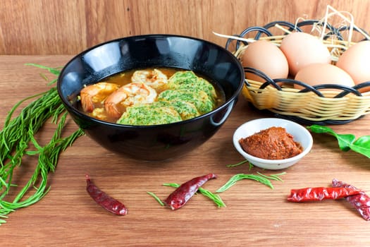 Hot and sour soup curry with shrimps and acacia pennata omelette. In black dish on wood table.