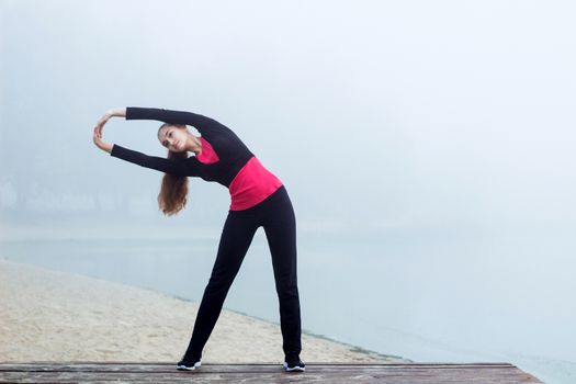 Young pretty slim fitness sporty woman does stretching exercises during training workout outdoor