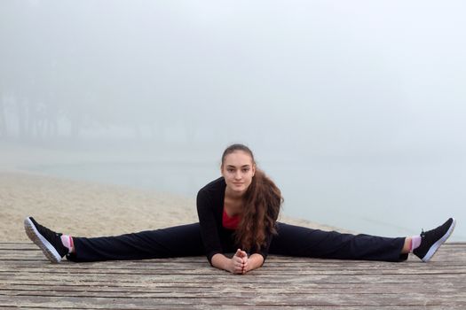 Young pretty slim fitness sporty woman does stretching exercises during training workout outdoor