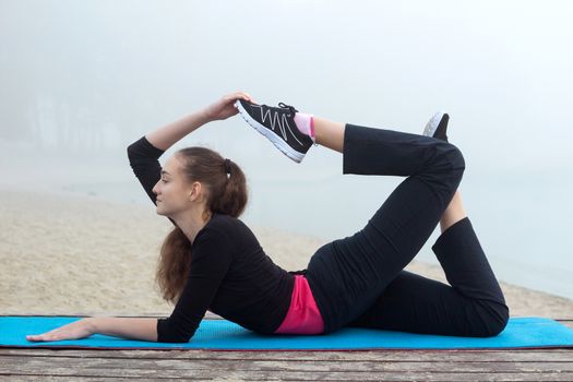 Young pretty slim fitness sporty woman does stretching exercises during training workout outdoor