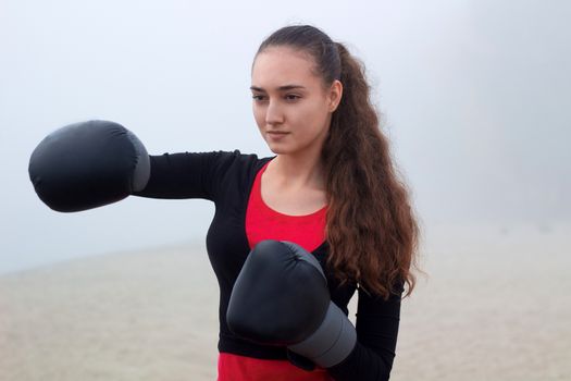 Young pretty slim fitness sporty woman does boxing exercises during training workout outdoor