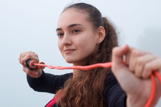 Young pretty slim fitness sporty woman doing streching exercise with rope during training workout outdoor