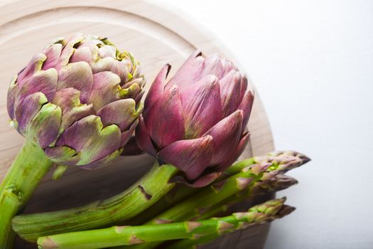 Artichokes and asparagus on a wooden board.