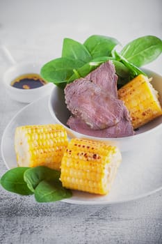 Beef and grilled corn with salad on a white plate