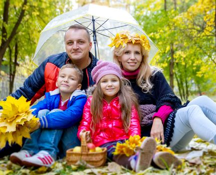 Happy family with two kids under umbrella and autumn leaves