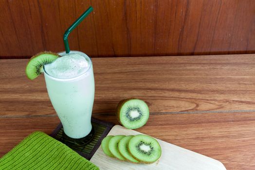 Healthy green smoothie made from kiwi with green straws on a wooden table.