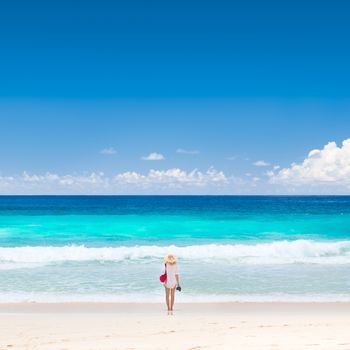 Lone woman wearing white tunic and beach hat, enjoying amazing view of Police Bay on Mahe Island, Seychelles. Summer vacations on picture perfect tropical beach concept.