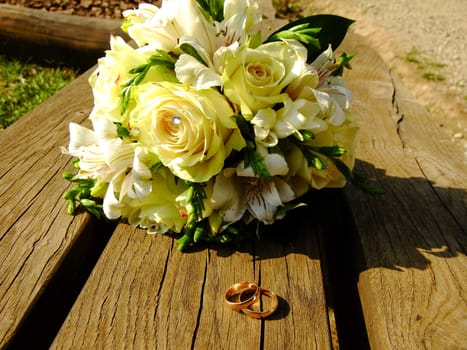 Beautiful white wedding Bouquet and two golden Rings on the Bench