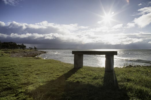 Bench with Ocean and a cloudy sky.