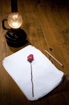 Old oil lamp, manuscript and rose on a wooden table