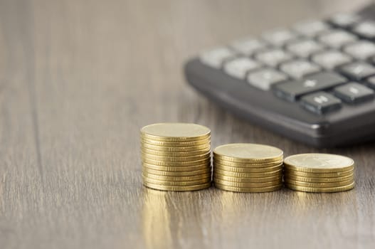 Close up step pile of gold coins have blur calculator on wood background.