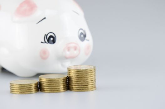 Close up step pile of gold coins have blur piggy bank on white background.