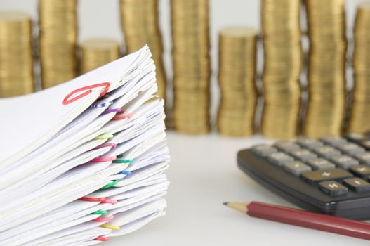 Close up pile paperwork of report and receipt with colorful paperclip have blur pile of gold coins and calculator with pencil as background.