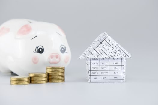 House and step pile of gold coins have blur piggy bank on white background.