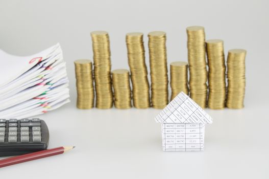 House have blur pile of gold coins with pile paperwork of report and receipt with colorful paperclip and calculator with pencil on white background.