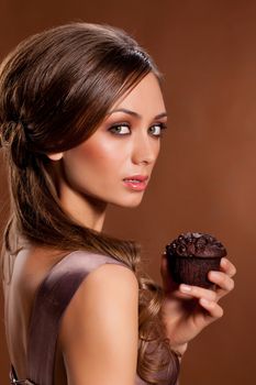 Young attractive woman holding a chocolate cake on a studio brown background