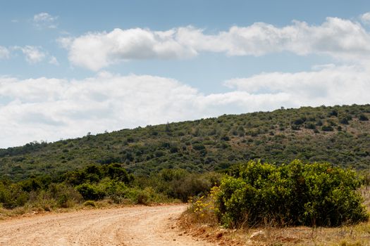 Clouds in the Skies with a green hill and road that leads to ...