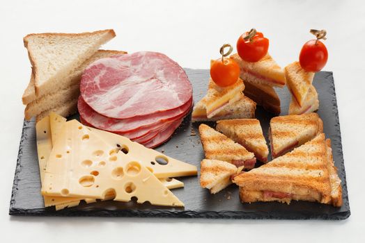 Slices of cheese, ham, bread and hot marinated cherry tomatoes sandwiches on a slate board