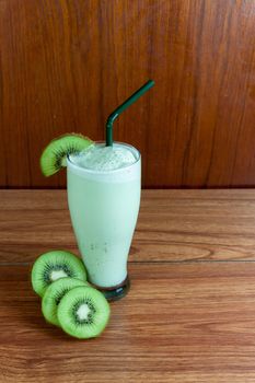 Healthy green smoothie made from kiwi with green straws on a wooden table.