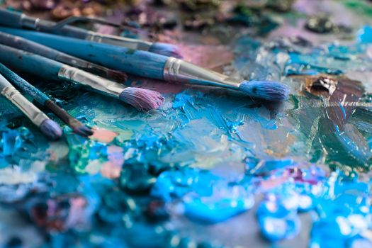 artists brushes and oil paints on wooden palette. macro artist's palette, texture mixed oil paints in different colors and saturation. palette with paintbrush and palette-knife