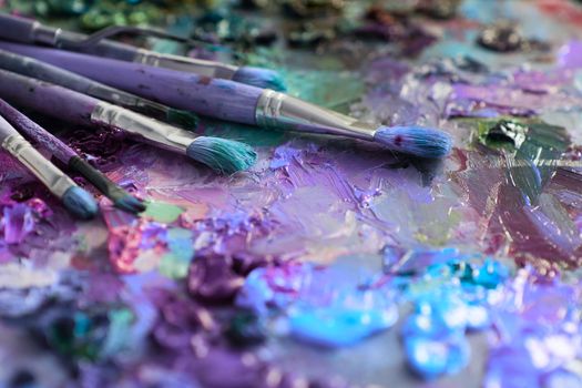 artists brushes and oil paints on wooden palette. macro artist's palette, texture mixed oil paints in different colors and saturation. palette with paintbrush and palette-knife