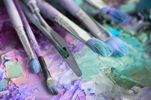 artists brushes and oil paints on wooden palette. macro artist's palette, texture mixed oil paints in different colors and saturation. palette with paintbrush and palette-knife. Brushes on canvas