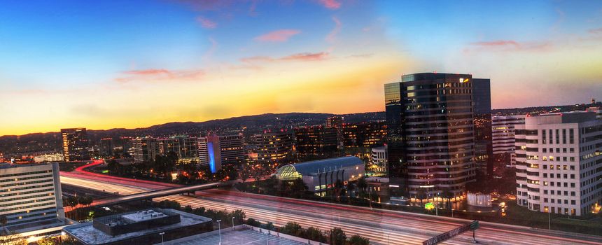 Sunrise over a highway in Irvine, California as headlight trails move through the roadways.