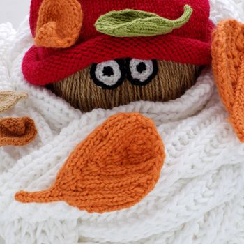 Diy funny, humor Christmas background handmade with lazy snowman from white scarf, red hat, eye and group of knitted leaf from yarn, winter leaves drop on head in cold day, art design for Xmas holiday