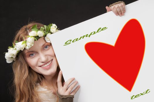 A smiling beautiful woman with white roses wreath in her long hair is holding a sign with red heart and a clipping path.
