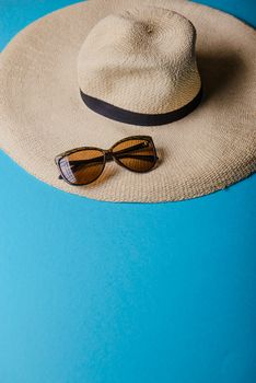 Straw hat and sunglasses on blue background. beach equipment.