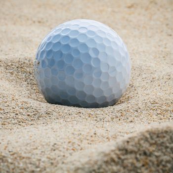 Close up golf ball in sand bunker shallow depth of field. A golf ball plugged deep in sand trap.