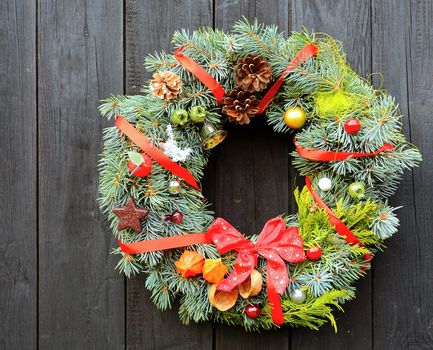 Christmas handmade decorative wreath with small ornaments and red ribbons on wooden background.