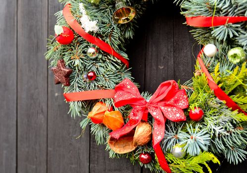 Christmas handmade decorative wreath with small ornaments and red ribbons on wooden background.