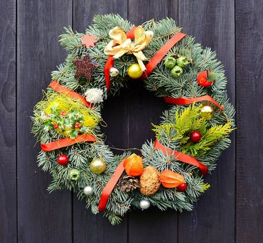 Christmas handmade decorative wreath with small ornaments and red ribbons on wooden background.