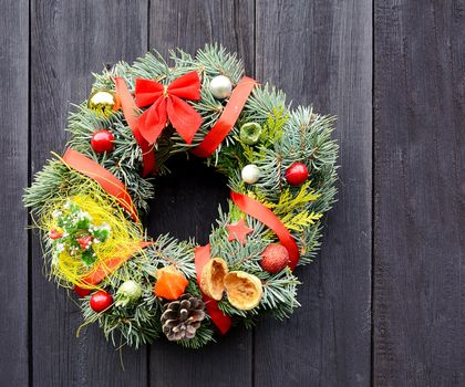 Christmas handmade decorative wreath with small ornaments and red ribbons on wooden background.