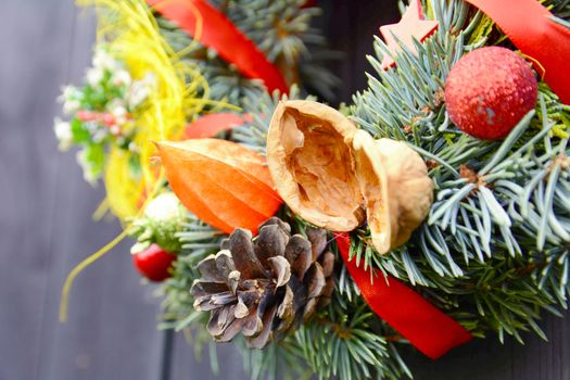 Christmas handmade decorative wreath with small ornaments and red ribbons on wooden background.