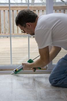 Contractor caulking around glass door frame, sealing from possible air leaks, conserving energy