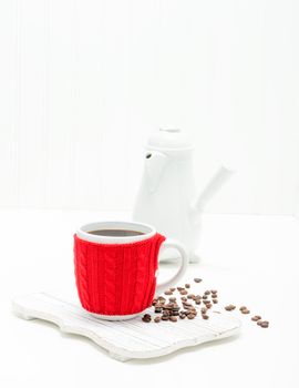 Fresh brewed coffee in a cup with a bright red cozy to keep it warm.