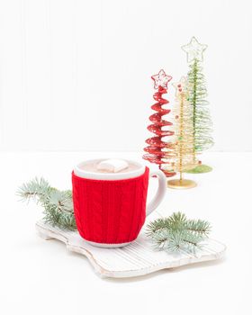 Hot chocolate in a white ceramic cup with a red cozy to keep it warm.