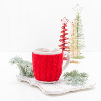 Hot chocolate in a cup with a bright red cozy to keep it warm.