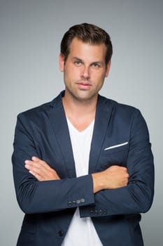 Portrait of a smart young man standing with arms crossed against gray background