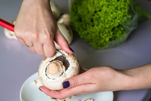 hands clean mushrooms with a knife over a white plate