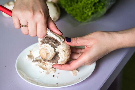 hands clean mushrooms with a knife over a white plate