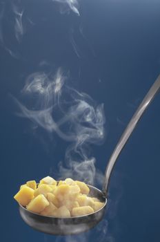 Hot boiled potatoes in the ladle, diced. Blue background, from hot vegetables, steam rises.Selective focus.