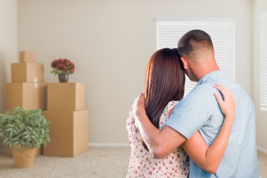 Young Military Couple Facing Empty Room with Packed Moving and Potted Plants.