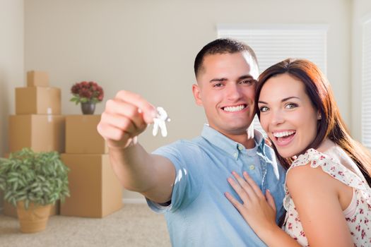 Happy Young Military Couple with House Keys in Empty Room with Packed Moving and Potted Plants.