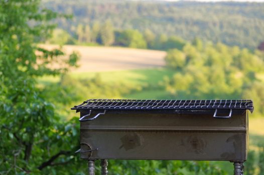 a empty portable BBQ grill in front of a fresh green summer landscape