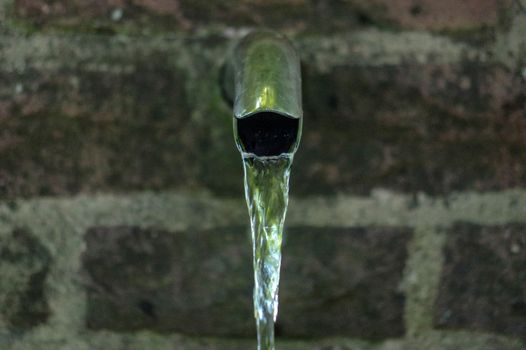 Close up of running water from a tap with brick wall in background