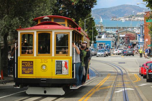 San Francisco, California - Mai 23, 2015: Lot Tourists riding on the iconic cable car, blue sky day at top of Hyde Street view overlooking the bay water and Alcatraz prison