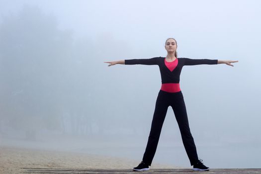 Young pretty slim fitness sporty woman does yoga exercises during training workout outdoor